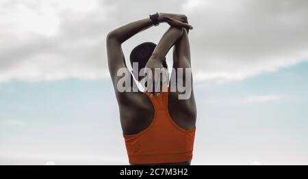 Rear view of woman doing hand stretching exercise. Female athlete working out outdoors against sky. Stock Photo
