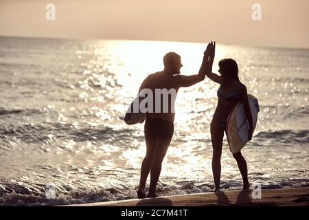 young surfers passing by on the beach with high five greeting, smiling Stock Photo