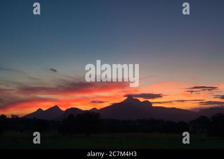 The peak of Mount Warning just right of centre named by Captain Cook, silhouetted at sunset on the mid east coast of New South Wales, Australia. Stock Photo