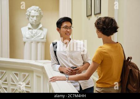 Two young attractive casual international students happily talking at break in university Stock Photo