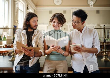 Group of young casual multinational students happily studying with book together in library of university Stock Photo