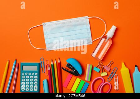 School supplies with medical mask and sanitizer on orange background Stock Photo