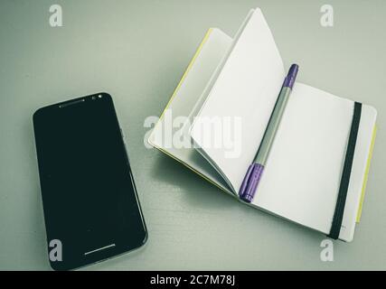 Closeup shot of a notebook with a grey and purple pen on it next to a phone Stock Photo