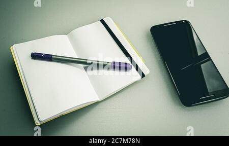 Closeup shot of a notebook with a grey and purple pen on it next to a phone Stock Photo