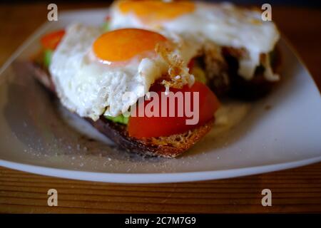 Closeup selective focus shot of a sandwich with fried eggs on top on a white plate Stock Photo