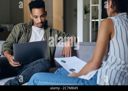 Young handsome casual African American man with laptop working with colleague on new project in co-working space Stock Photo