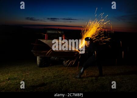 Agricultural worker using angel grinder at night. Stock Photo