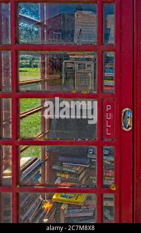 Disused Norfolk village red BT phone box used as a library. Door closed. View of books stored untidily inside Telephone in view Portrait format Stock Photo