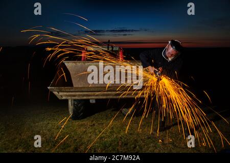 Agricultural worker using angel grinder at night. Stock Photo