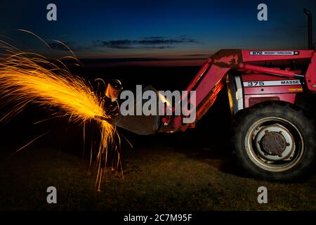 Agricultural worker using angel grinder at night. Stock Photo