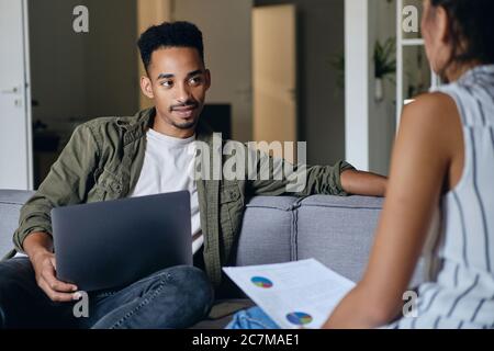 Young attractive African American man with laptop working with colleague in co-working space Stock Photo
