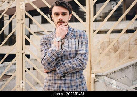 Young handsome man in checkered jacket wistfully looking in camera on street Stock Photo