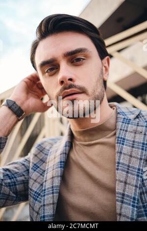 Portrait of attractive stylish man in checkered jacket dreamily looking in camera outdoor Stock Photo