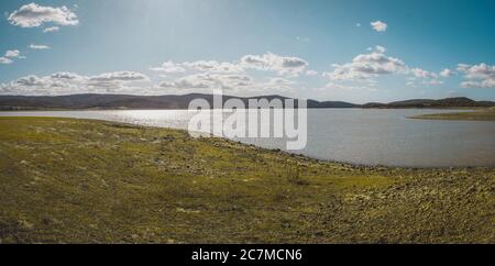Wide shot of a beautiful lake surrounded by mountains with a cloudy blue sky in the background Stock Photo