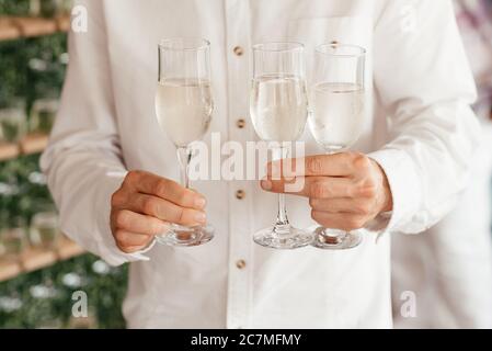 Faceless man wearing white shirt holding three champaagne glasses in his hands
