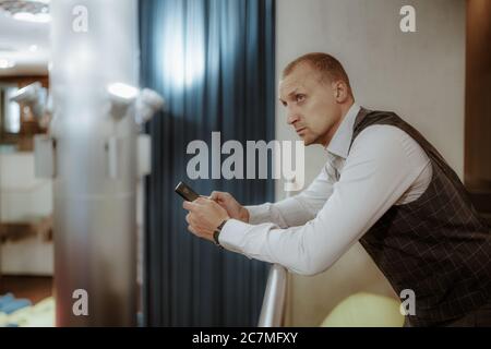 A stately mature man entrepreneur is pensively looking aside while leaning against the balcony railing of a modern office chillout area Stock Photo