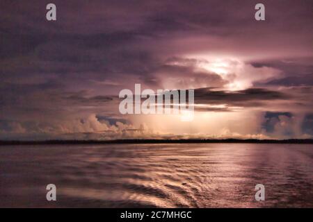 Sheet lightning amongst the clouds at night over the River Amazon illuminating the dark storm clouds from within Stock Photo