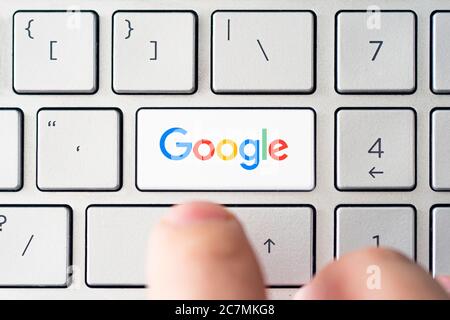 The male presses a button on the keyboard with the Google logotype. Google is USA multinational corporation specializing in Internet-related services. Stock Photo