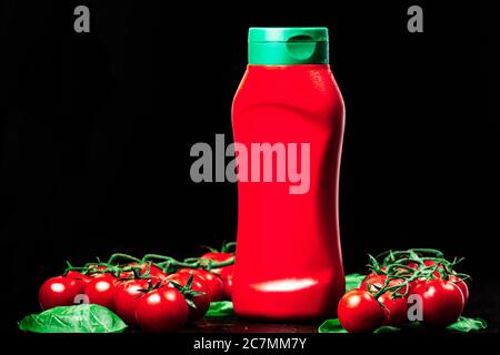 bottle, tube of red ketchup with a green cap and two ripe branches of cherry tomatoes with spinach on a black background. close up, horizontal orienta Stock Photo