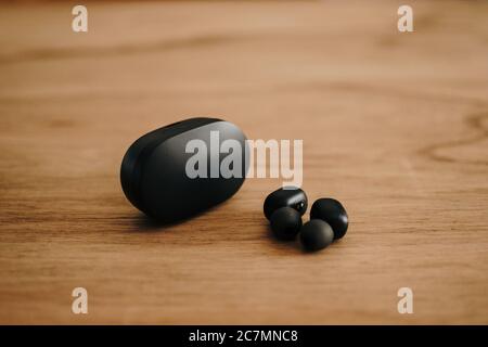 Closeup shot of two modern, wireless, black earbuds and a black earbud case on a wooden surface Stock Photo
