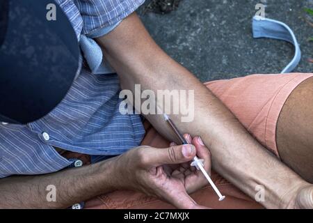 Hands of a drug addict with a syringe full of narcotic, heroin or cocaine to the arm veins. Drugs addiction and obsession. Close up. Stock Photo