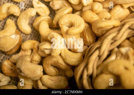 Cashew nuts in a wicker basket and cashew nuts scattered on burlap with a rough texture surface texture. Close up Stock Photo