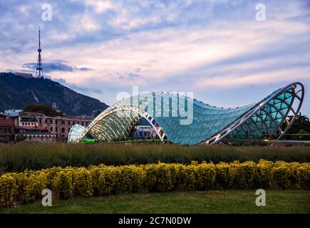 Bridge of Peace against the background of Mount Mtatsminda and the TV tower. Tbilisi cityscape in the evening at sunset Stock Photo