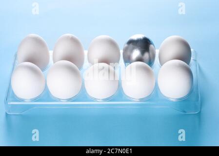 Silver egg standing out from crowd of plenty identical white eggs in plastic box background. Leadership, uniqueness, independence, idea, initiative,strategy, dissent, think different, business success Stock Photo