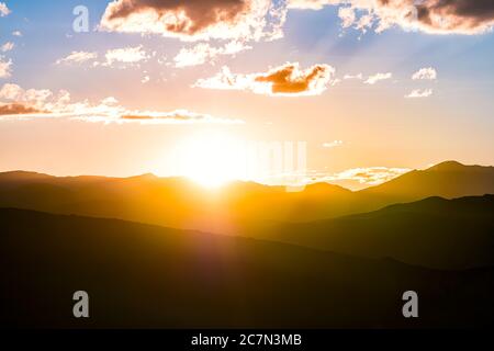 Yellow orange colorful sunset with sun rays flare in Aspen, Colorado USA with aerial view on Rocky Mountains Peak mountain ridge silhouette clouds at Stock Photo