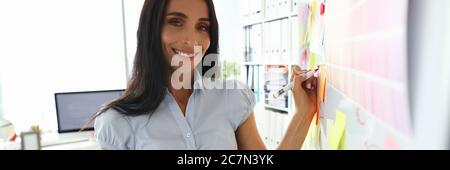 Beautiful smiling brunette caucasian woman writing something on whiteboard Stock Photo