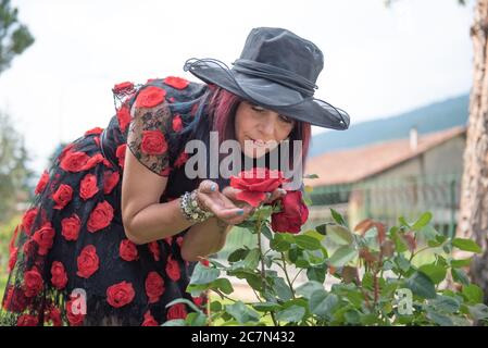Woman sniffs the aroma of beautiful red rose bushes in a botanical garden. Stock Photo