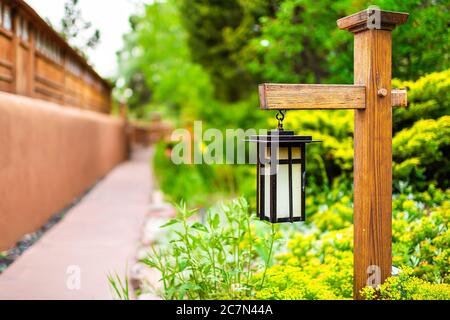 Japan hanging lantern lamp light on wooden post in Japanese garden with path by house temple and green foliage background Stock Photo