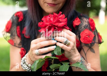 Woman sniffs the aroma of beautiful red rose bushes in a botanical garden. Stock Photo