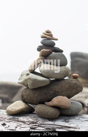 Rocks balanced on a log on a beach in Yachats, Oregon, USA. Stock Photo