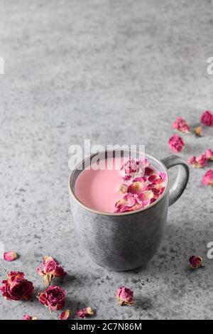 Rose moon milk in grey cup and rose petals on grey background. Vertical format. Stock Photo