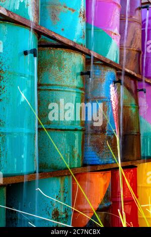 Modern, colorful fountain made from vintage, painted industrial drums stacked on top of each other with water trickling from open spigots. Stock Photo