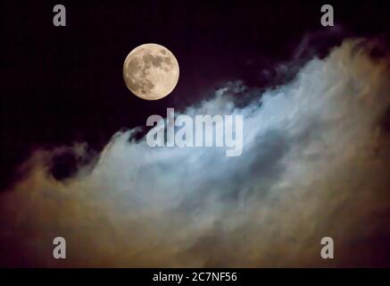 A full moon illuminates passing clouds in a night sky. Stock Photo