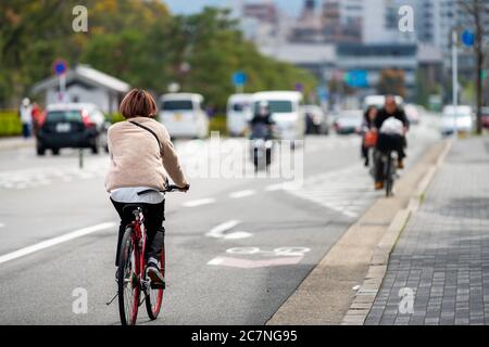 Kyoto, Japan - April 17, 2019: Japanese person back on bicycle riding bike on street candid city life with traffic cars road near station Stock Photo