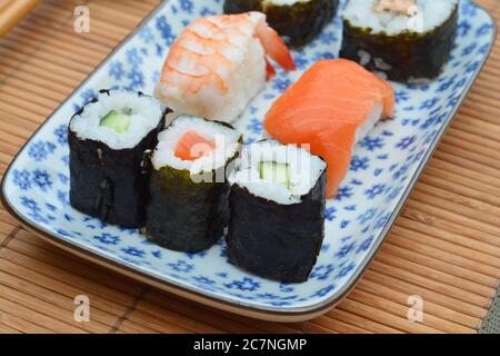 Closeup shot of sushi rolls in a plate with floral patterns on a bamboo table cover Stock Photo