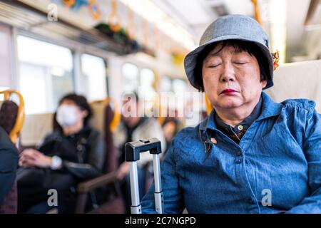 Nara, Japan - April 15, 2019: People sitting inside train riding public transportation from Nara to Kyoto with Japanese woman sleeping closeup candid Stock Photo