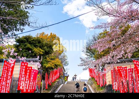 Nara, Japan - April 15, 2019: People walking on steps stairs up with red flags banners to Kofuku-ji temple in downtown city wide angle view and blue s Stock Photo