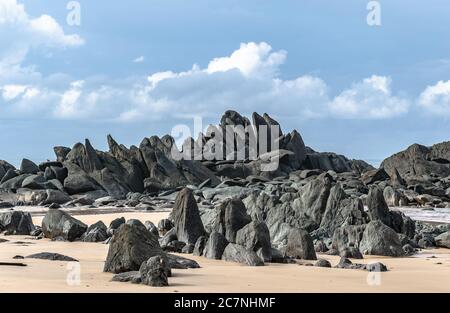 Black dark boulders lying on a beach after the coast in Axim Ghana West Africa Stock Photo