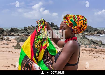 Ghana woman on the beautiful beach of Axim, located in Ghana West Africa. Headdress in traditional colors from Africa. Stock Photo