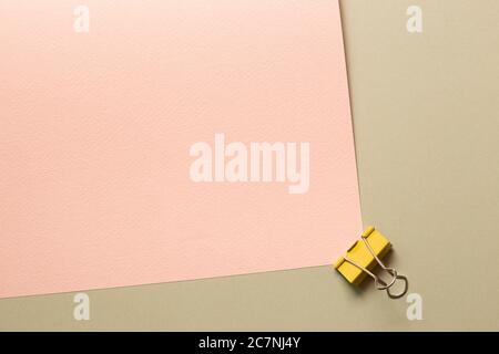 Yellow metal binder clip on pink and beige background. top view Stock Photo