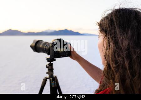 Bonneville Salt Flats white background near Salt Lake City, Utah at colorful sunset with woman photographer taking picture of view using camera on tri Stock Photo
