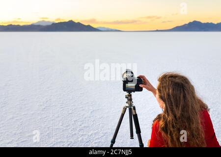Bonneville Salt Flats white color near Salt Lake City, Utah at colorful sunset with woman photographer taking picture of view using camera on tripod Stock Photo