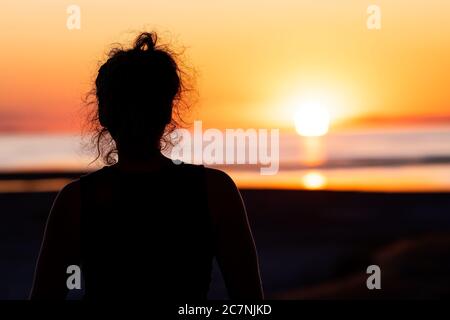 Woman back watching sun path reflection sunset on Great Salt Lake in Antelope Island State Park with water surface and silhouette of person near campg Stock Photo