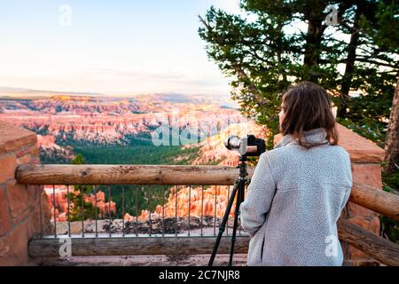 Woman taking pictures photos of view from Bryce Point overlook of hoodoos rock formations in Bryce Canyon National Park at sunset with tripod and came Stock Photo