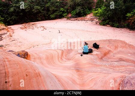 Zion National Park in Utah on Gifford Canyon trail with woman sitting resting by red sandstone formations rock in summer above high angle view Stock Photo