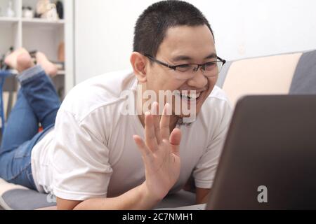 Asian man doing a video call at home, smiling to camera and waving. Happy cheerful expression Stock Photo